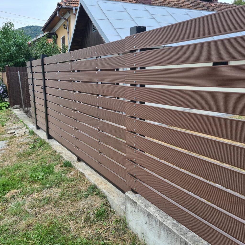 Scândură gard WPC maro fixată cu șuruburi pe stâlpi metalici.